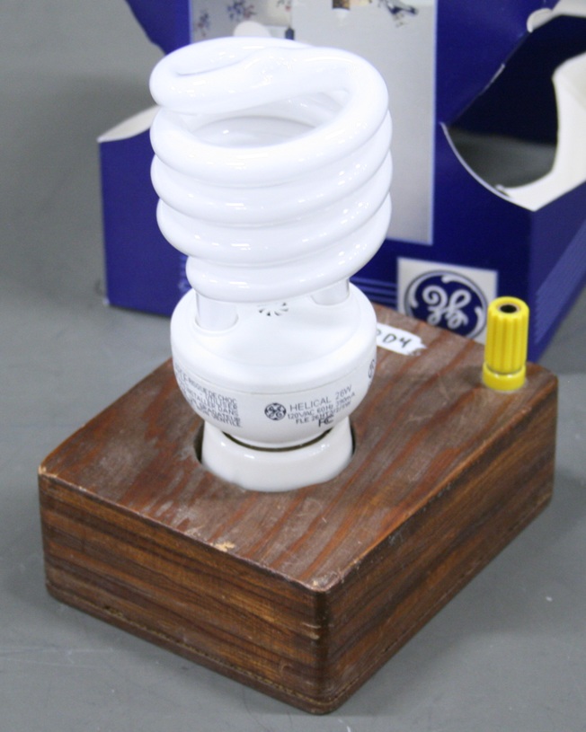 Coiled fluorescent bulb mounted in a square wooden base.