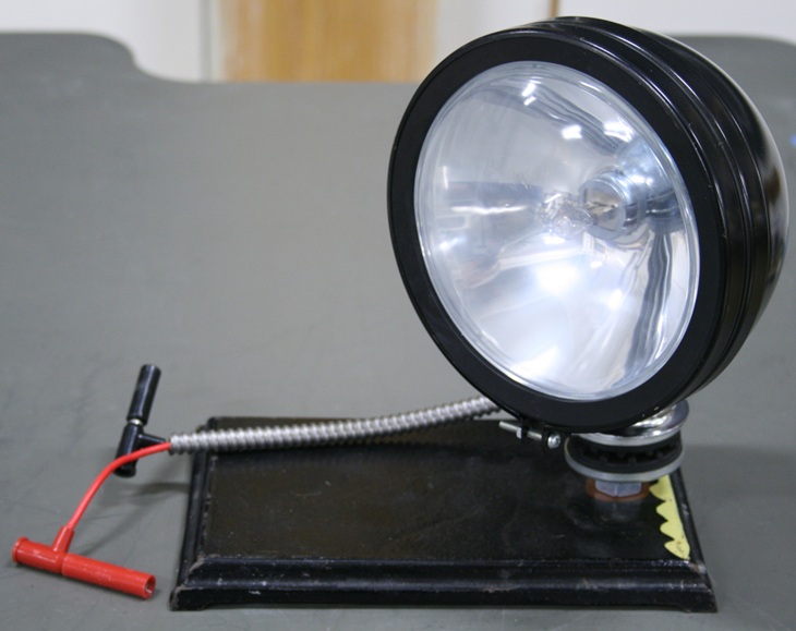 Motorcycle headlight mounted on a ring stand base, with short banana cables.