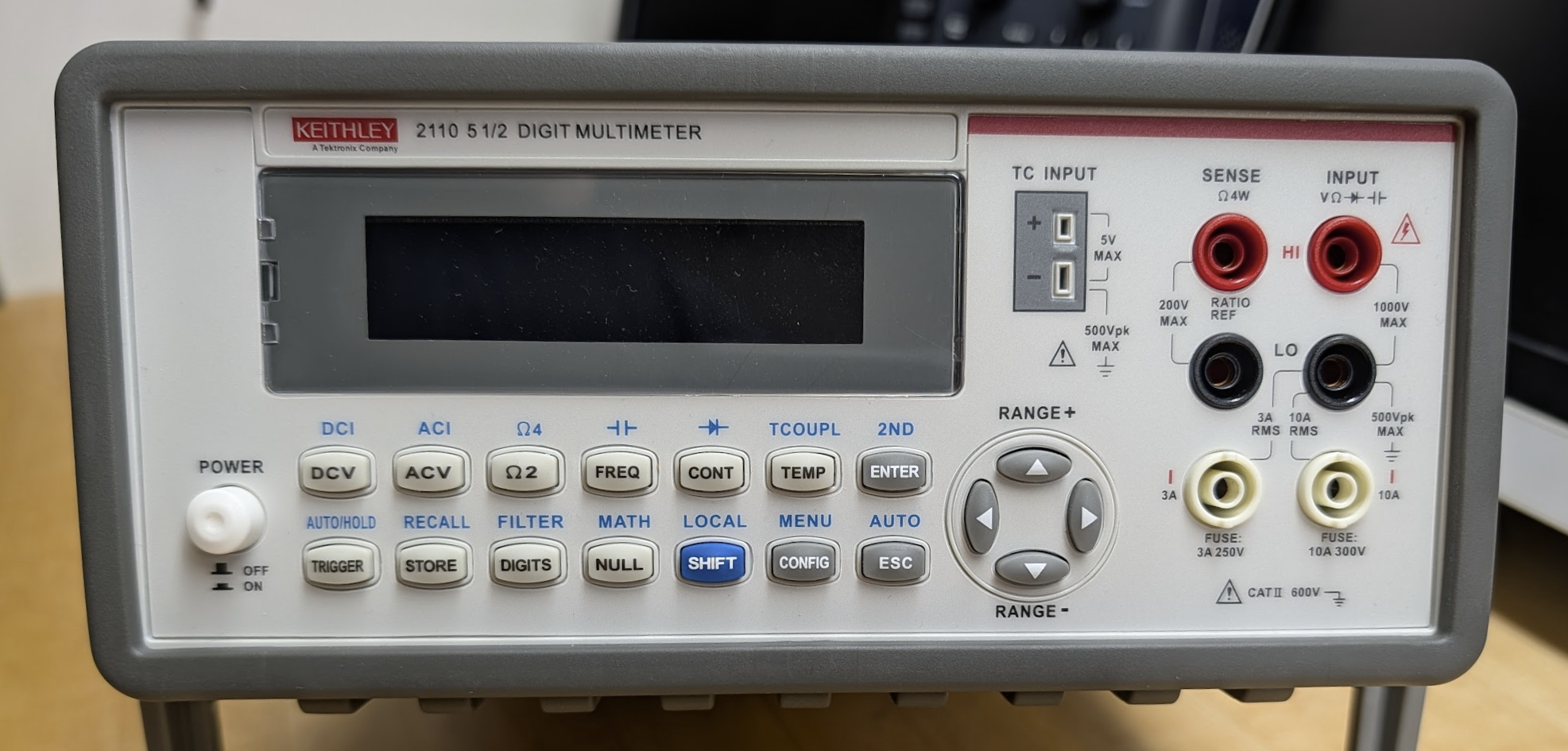 Benchtop digital multimeter with a large central display, rows of function buttons, directional range pad, and front-panel measurement input terminals.