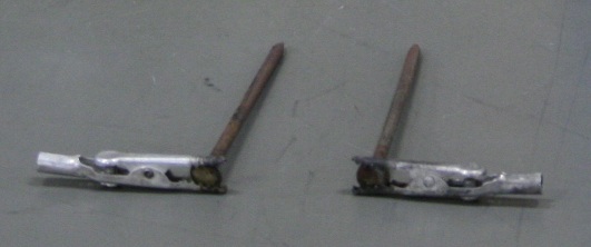Two alligator clips, each holding a three-and-a-half inch nail at right angles.