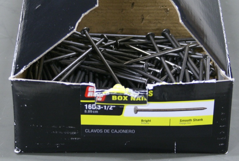 Open cardboard box mostly full of 3.5 inch box nails.
