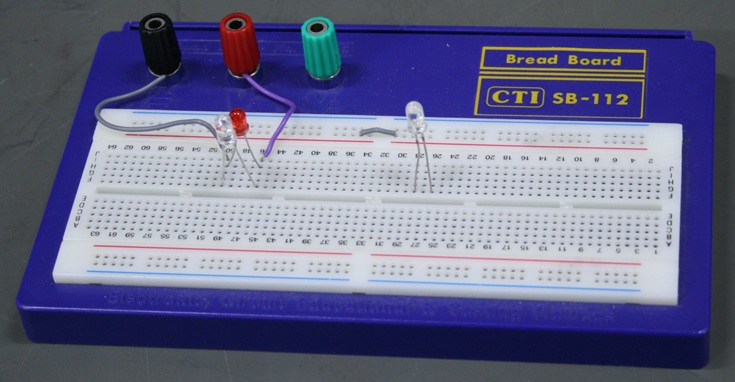 Plastic breadboard with 3 LEDs and 3 terminals.  Two LEDs are wired oppositely in parallel to the plus and minus terminals.