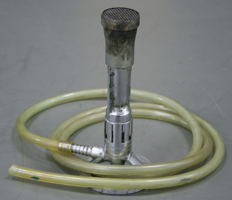A laboratory burner about a handspan high with an inch-wide grid-covered opening.  It sits in a coil of rubber hose attached to the barb at the burner's base.