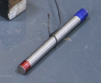 A cylindrical magnet two inches long and less than a quarter inch in diameter.  The ends are colored red for north and blue for south, and a thread is tied around the center.