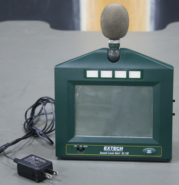 A self-standing rectangular case with a large LCD display, top-mounted microphone, and four LED volume indicators.