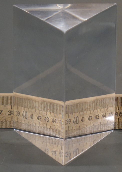 An equilateral prism 3 inches wide refracts a ruler placed along its rear face.