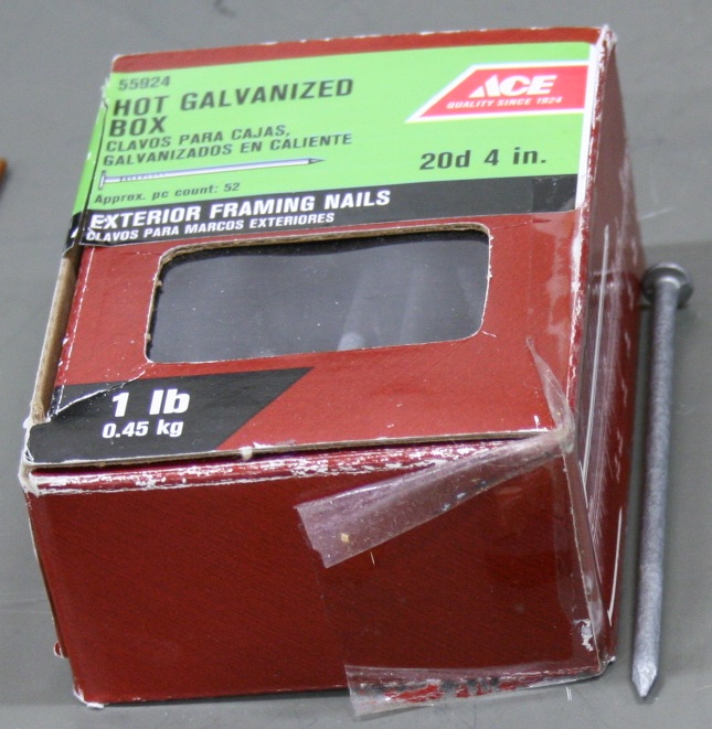 A one-pound box of four0inch hot galvanized box nails, with one of the nails beside it.