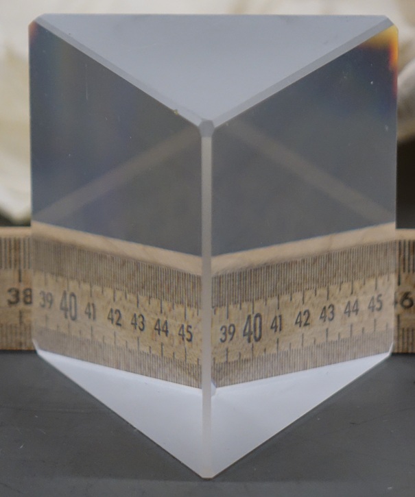 An equilateral glass prism 3 inches wide refracts a ruler placed along its rear face.