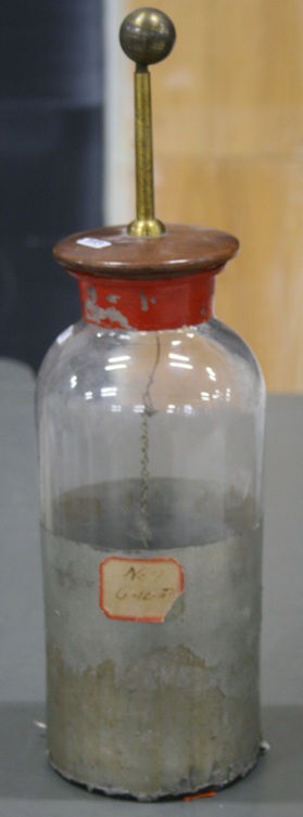 A glass jar roughly the size of a water bottle, with the lower half lined inside and out with metal foil.  A wooden plug supports a metal ball on top of a brass rod, and a chain dangles inside the jar.