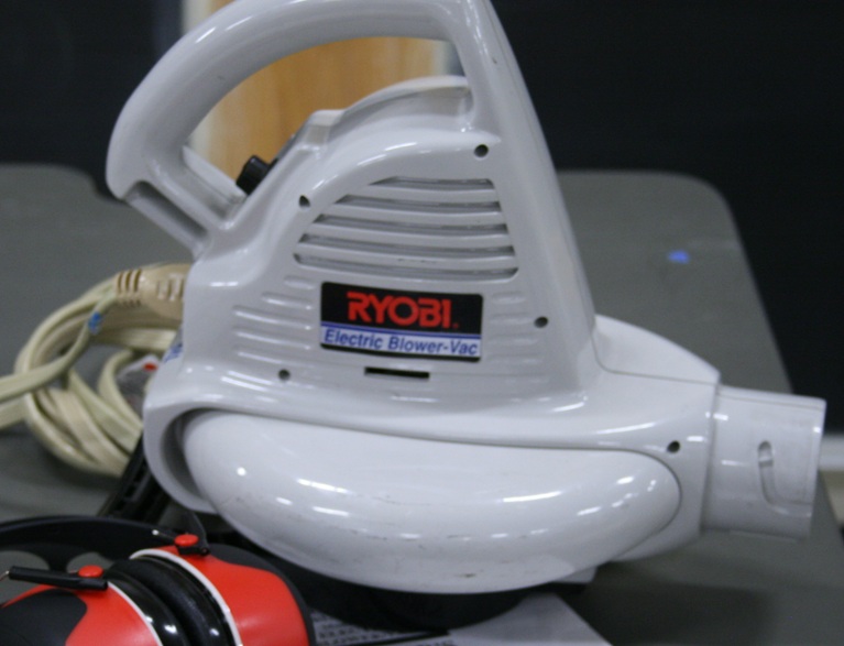 A leaf blower without any nozzle attachments sits next to a set of ear protectors.