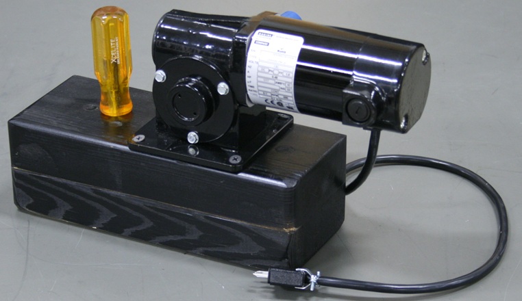 A cylindrical motor is mounted on a wood block like a cannon.  A nut driver is stored in the block behind the motor.