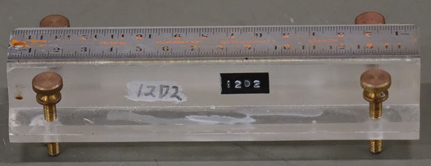 A metal ruler twelve centimeters long mounted on a plastic block.