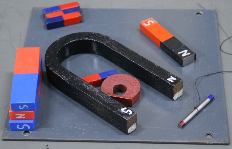 A thin steel plate 8 inches square holds several magnets of different types: a large and small horseshoe magnet, four bar magnets an inch long, a three-inch bar magnet, and a trio of three-inch series magnets in plastic cases.