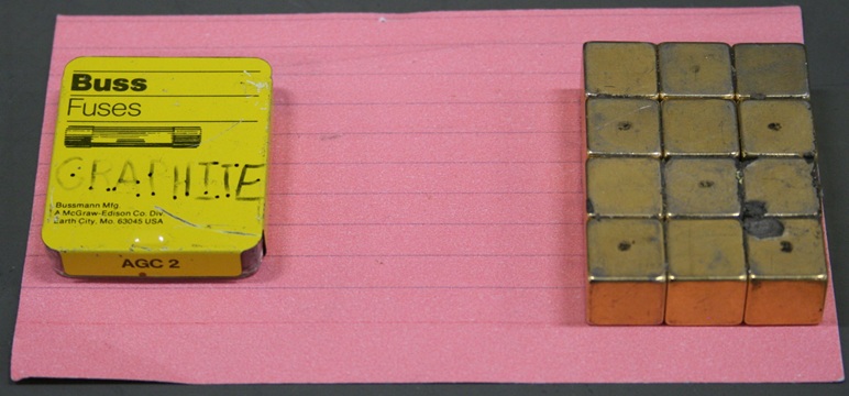 A metal fuse container and a 3 by 4 array of cube magnets rest on a pink index card.