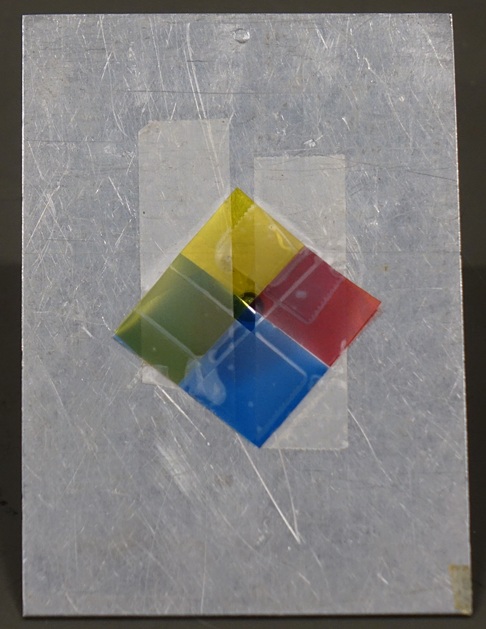 An aluminum plate, slightly larger than an index card, with a hole-punch sized opening in the center.  Colored cellophane over the hole divides it into red, yellow, green, and blue quadrants.