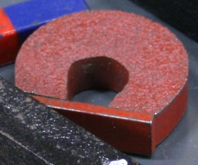A near-circular horseshoe magnet about an inch across with a thin iron bad connecting its poles.