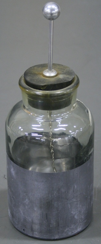 A glass jar a little larger than a soda can.  The lower half is lined inside and out with metal foil.  A rubber plug supports a metal ball on top of a rod, and a chain dangles inside the jar.
