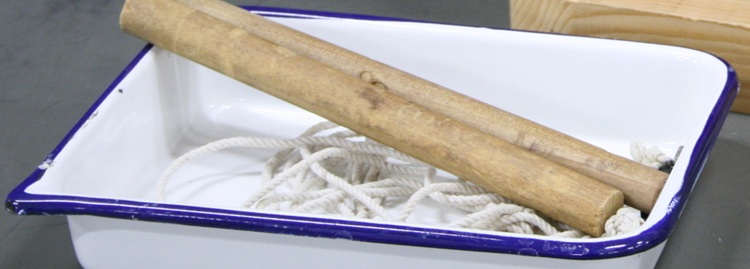 An enameled steel trat eight by six inches and an incha nd a half deep, containing two wooden dowels and a wad of string.