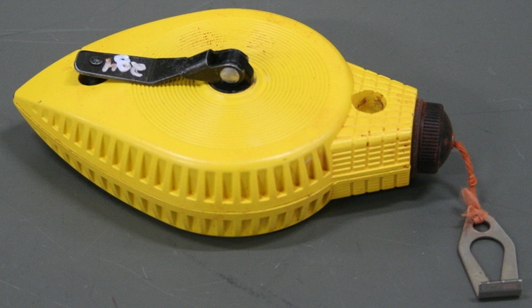 A drop-shaped handheld metal casing emits chalked string from the blunt end and has a crank handle for controlling its length.