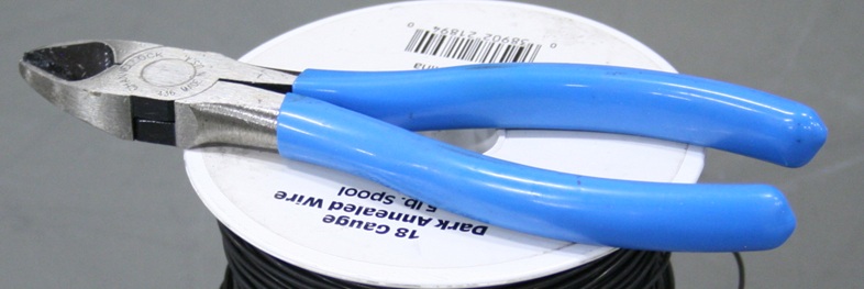 A pair of wire cutters with insulated handles, resting on a spool of iron wire.