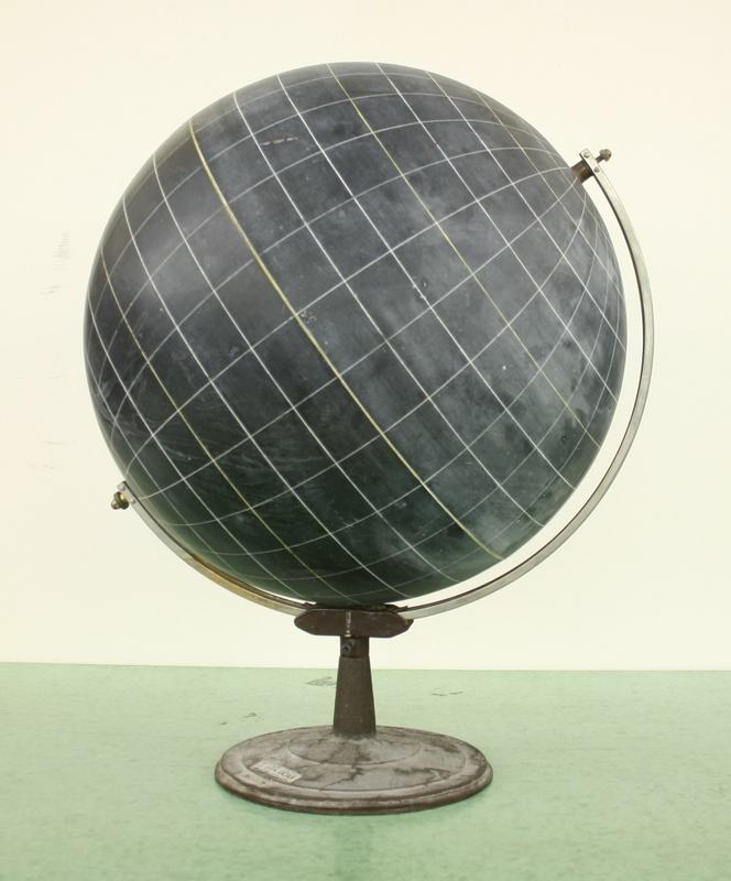 Dark slate globe with white latitude and longitude grid lines, mounted on a metal meridian arc bracket with ornamental cast iron pedestal base