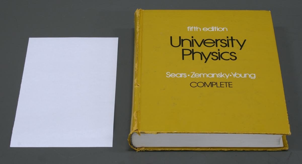 Yellow university physics textbook by Sears, Zemansky, and Young, fifth edition, placed next to a white sheet of paper on a gray surface