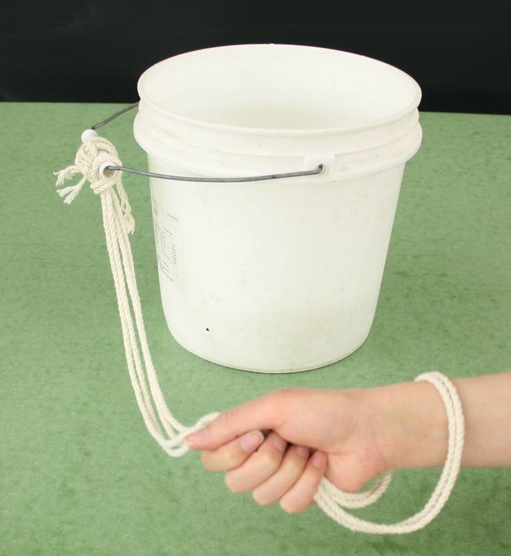 White plastic bucket with wire handle and rope threaded through it, looped around a person's wrist and hand for secure grip