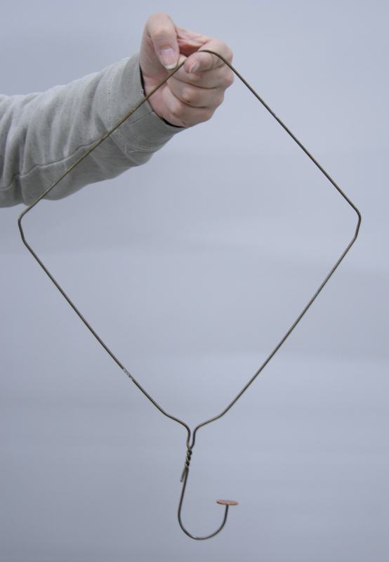 Hand holding a wire coat hanger bent into a diamond shape, with a penny balanced on the curved hook at the bottom