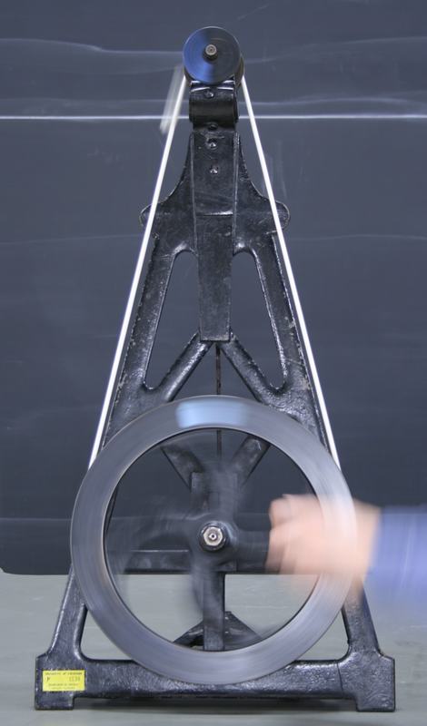 Centrifugal machine in operation with a hand turning the large wheel; the top pulley shows motion blur from its higher rotational speed