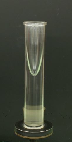Tall cylindrical glass vessel containing water, photographed against a dark background, showing a concave parabolic surface at the top of the water column