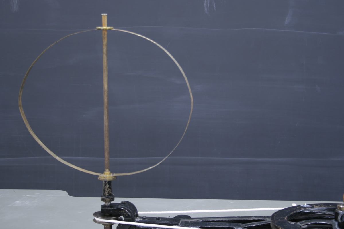 Flexible metal hoop at rest on a brass rod mounted on the centrifugal machine base, showing its circular shape