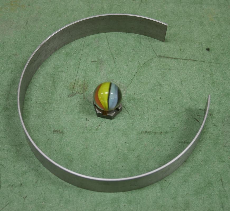 Aluminum 3/4 ring (open at top) with a multicolored glass marble sitting at center, on a green lab bench surface