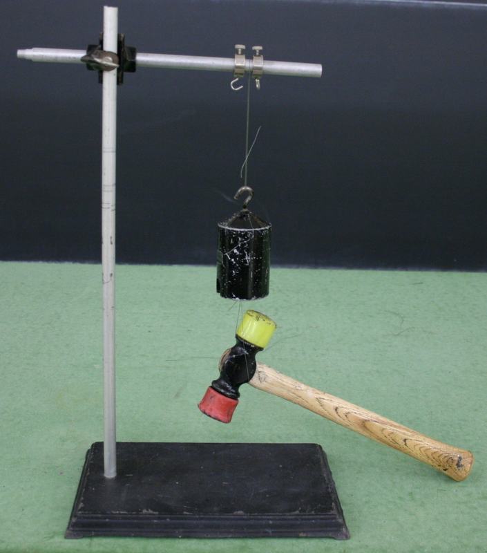 Ring stand with horizontal aluminum rod and hook; a black cylindrical 1 kg mass hangs from thread, with a hammer suspended below by a second thread