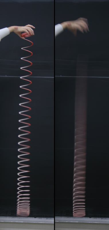 Side-by-side frames showing a hand holding a red plastic slinky suspended against a chalkboard (left) and the moment after release with the top collapsing while the bottom coils remain stationary (right)