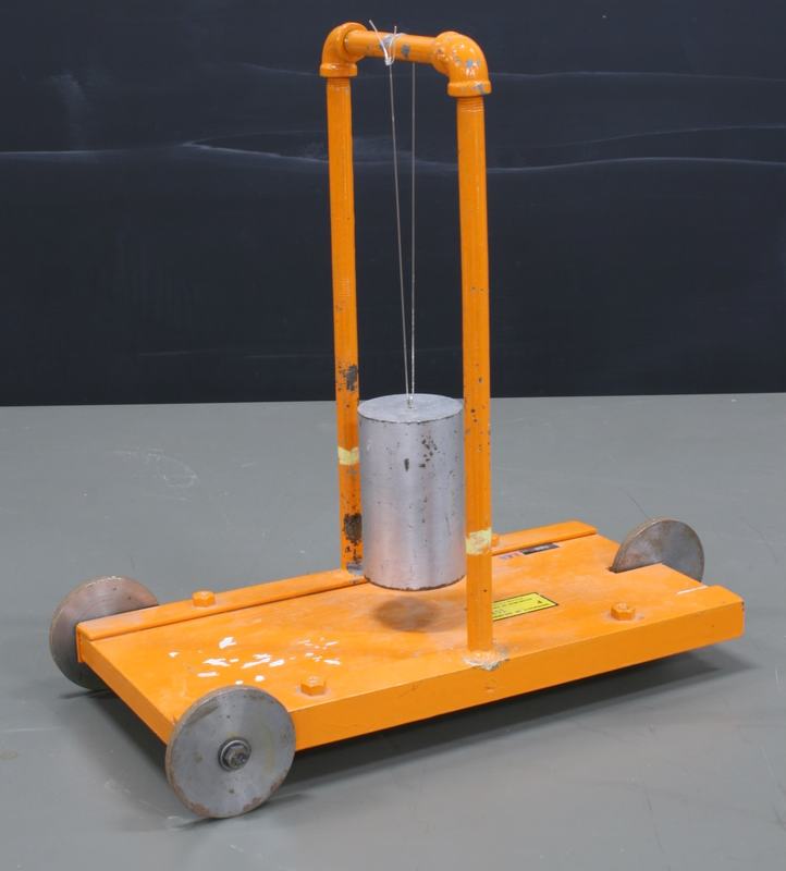 Orange painted metal cart with four silver wheels, two vertical pipes supporting an arched crossbar from which a heavy aluminum cylinder hangs by thin wires