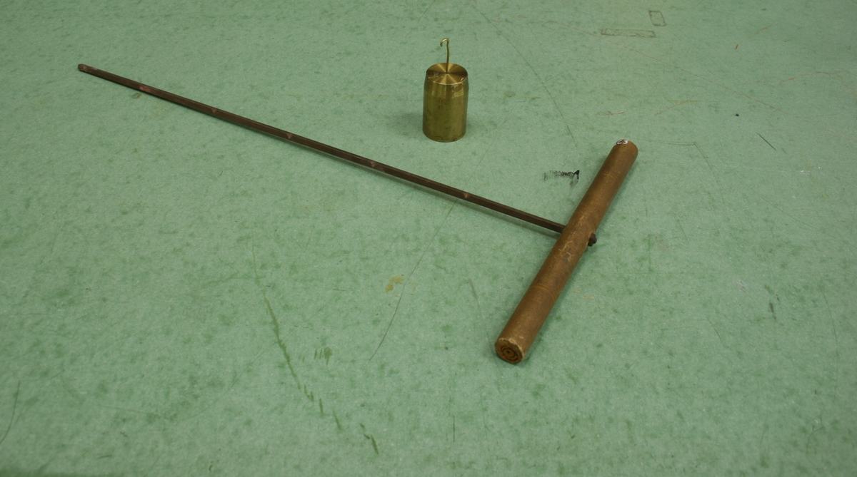 Torque bar apparatus on green surface: wooden cylindrical handle perpendicular to a thin metal rod with six equally-spaced notches, brass 1 kg hooked mass beside it