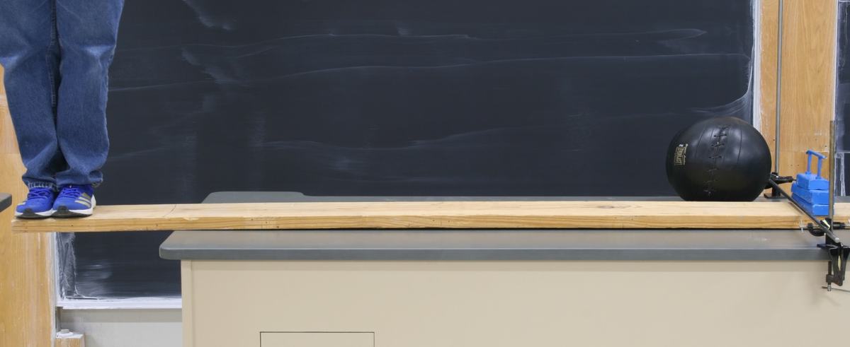Person at maximum extension on the overhanging plank, medicine ball counterweight near the far end