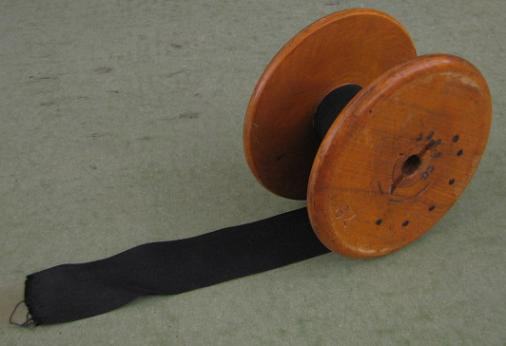 Large wooden spool with black ribbon wrapped around the inner hub, trailing out to the side