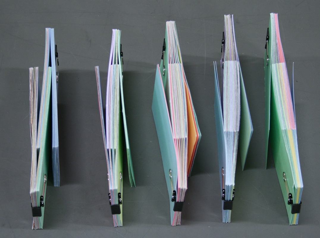 Five sets of interleaved pastel-colored index card stacks with black binder clips, hanging vertically and showing progressively more overlap from right to left