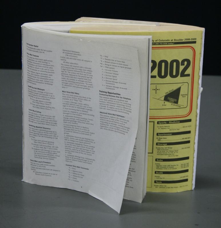 Two interleaved phone books — a white pages directory and a CU Boulder 2002 yellow pages — with pages shuffled together