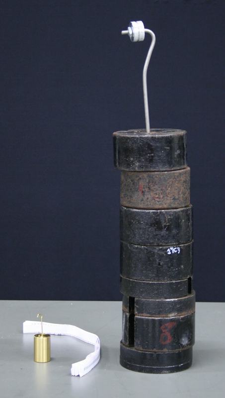 A tall stack of heavy iron disk masses on a mass hanger, with a small folded paper loop and a small brass mass shown beside it