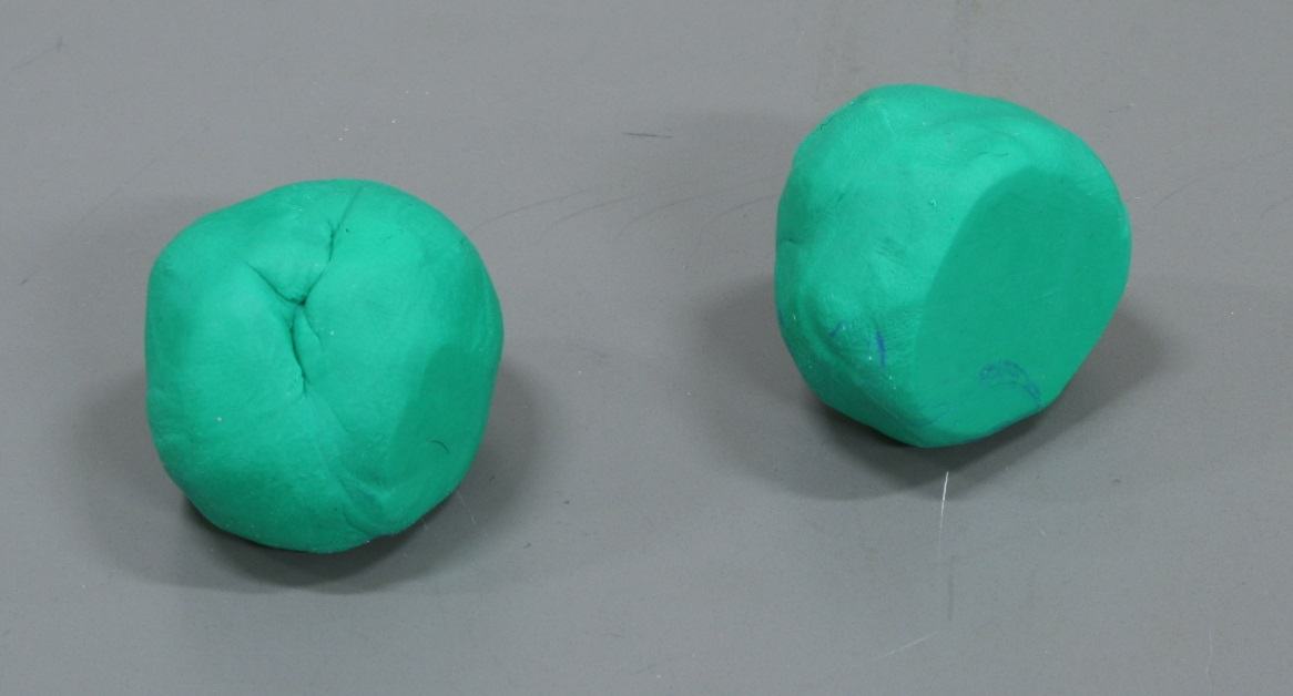 Two green modeling clay balls of similar size on a gray lab bench surface