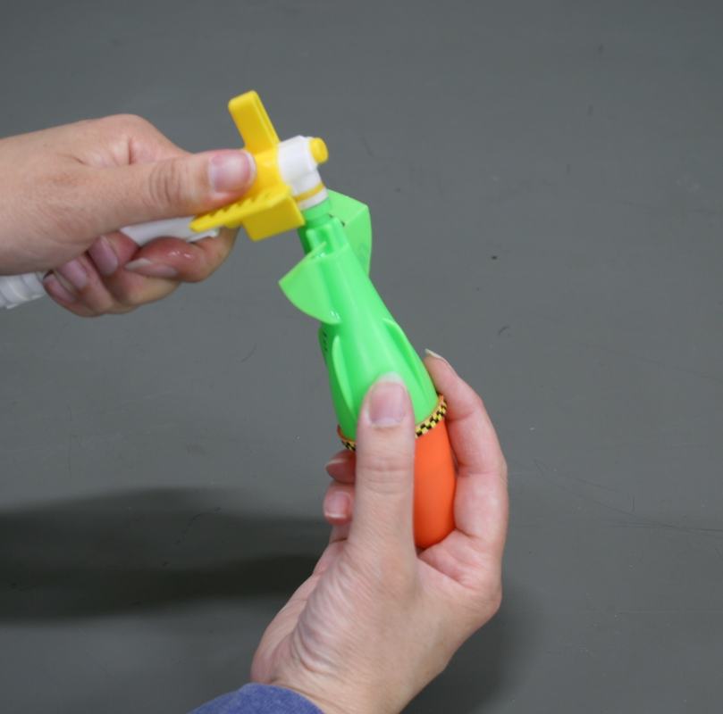 Hands inserting the white syringe pump into the tail of the inverted green rocket, with yellow lock ring visible