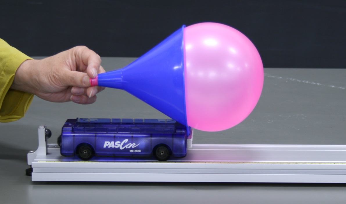 Hand holding the neck of an inflated pink balloon through a blue funnel mounted on a PASCO dynamics cart (blue bus-shaped, ME-6950) on an aluminum track