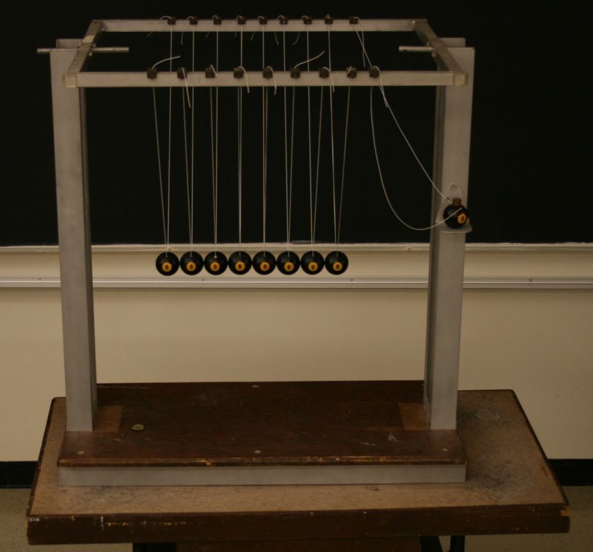 Large Newton's cradle with nine black billiard balls on bifilar suspension from a gray metal frame, mounted on a wooden base