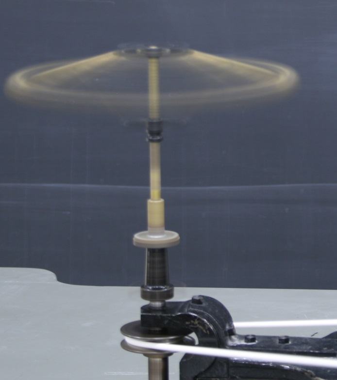 Centrifugal governor at high speed, brass balls nearly horizontal, motion-blurred, lower bar drawn fully upward