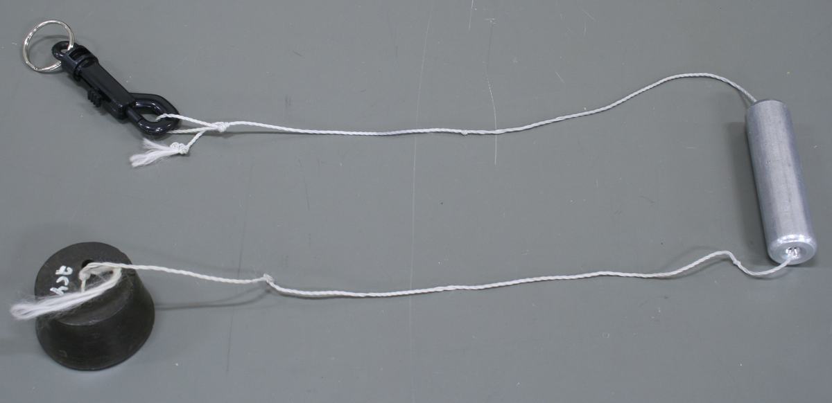 Apparatus laid out on a table: a black snap-hook clip with keyring, white string running to an aluminum cylinder on one end, and a dark rubber or lead hanging mass attached near the clip