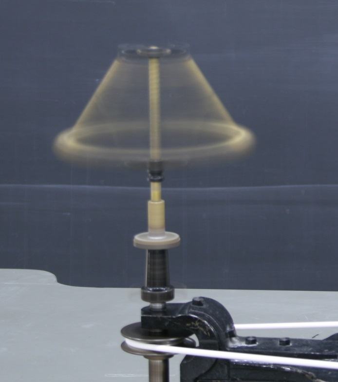 Centrifugal governor spinning at moderate speed, brass balls swung outward in a conical shape, motion-blurred