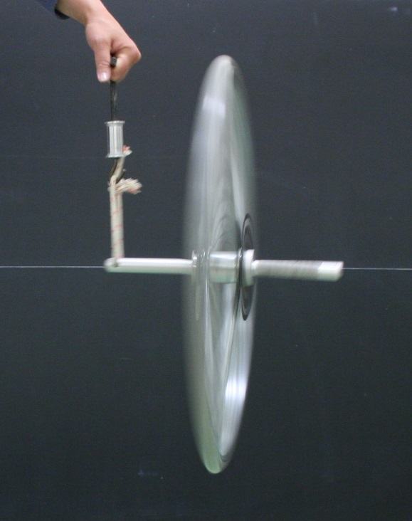 Spinning bicycle wheel suspended by a string from one end of the axle, showing motion blur of the wheel as it precesses under gravitational torque