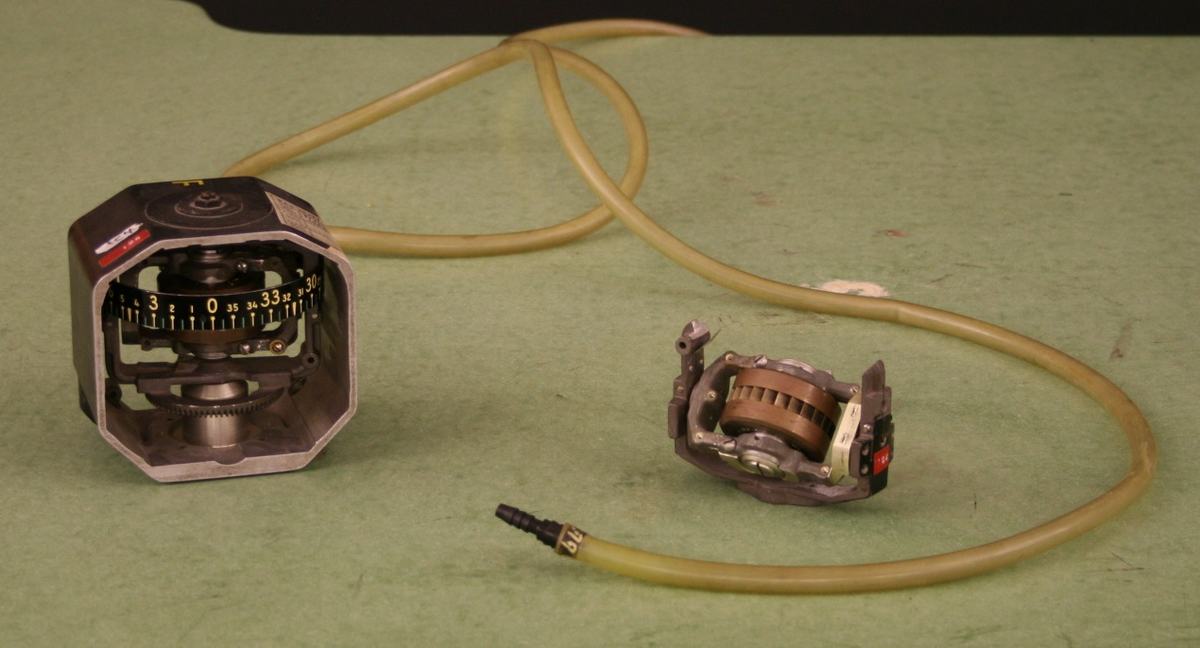 Two WWII aircraft gyroscope instruments: a heading indicator in its housing (left) and an exposed gyro rotor mechanism (right), connected by rubber air hoses with a barb fitting